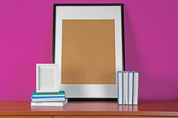 Books and frame on wooden table against pink background