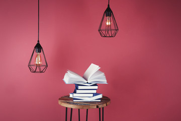 Little table with pile of books and decorative lamps on pink background