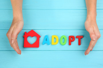 Female hands, word ADOPT and figure in shape of house on wooden background