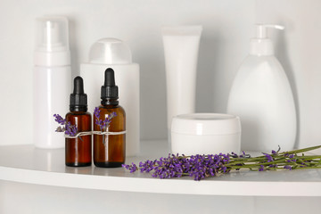 Bottles of essential oil with lavender on shelf in bathroom
