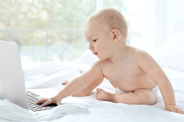 Cute baby boy with laptop on bed