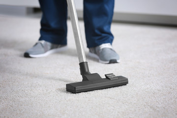 Legs of man hoovering carpet with vacuum cleaner