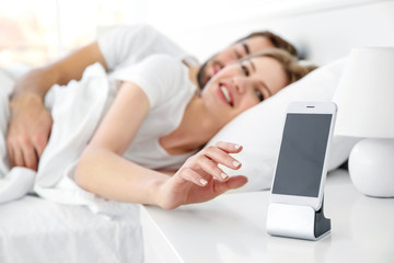 Happy couple waking up with mobile alarm clock