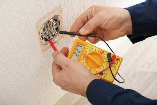 Electrician measuring voltage of socket in new building, closeup