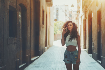 Beautiful curly woman talking with her sister while standing on street in summer day, smiling...