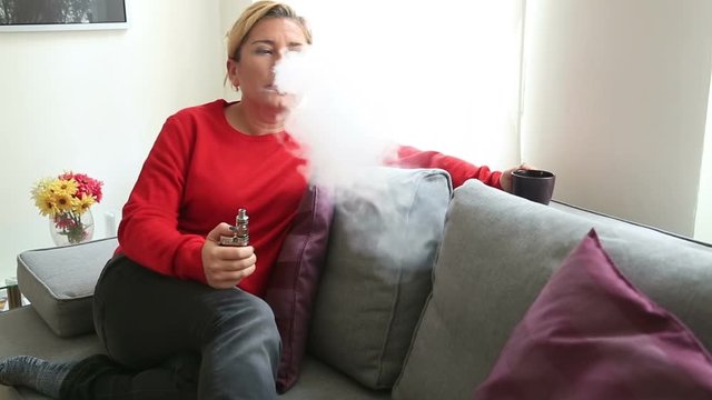 Portrait of a blonde woman relaxing indoors, smoking electronic cigarette e-cig