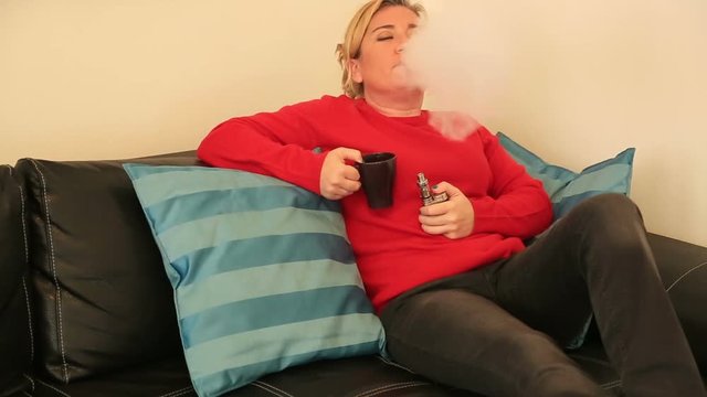 Portrait of a blonde woman relaxing indoors, smoking electronic cigarette e-cig