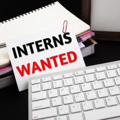Word text Interns wanted on white paper card on office table / business concept