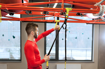 young sporty bearded man prepares for exersising in gym Adjust the length of the sling straps