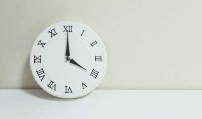 Closeup white clock for decorate show 4 o'clock on white wood desk and cream wallpaper textured background with copy space