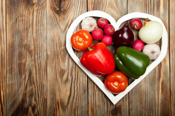 Vegetables. Peppers, tomatoes, garlic, onions, and radishes in the heart on rustic background