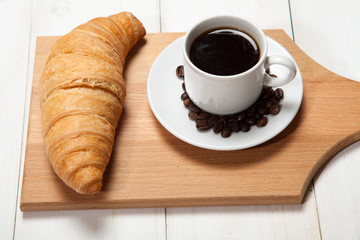 Cup of coffee and a croissant on a white wooden table