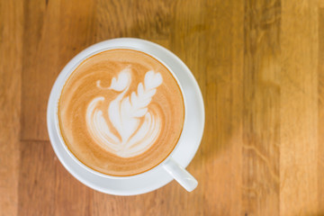 A cup of hot coffee late art on wood table in coffee shop with top view