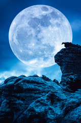 Boulder against blue sky with clouds and beautiful full moon at night. Outdoors.