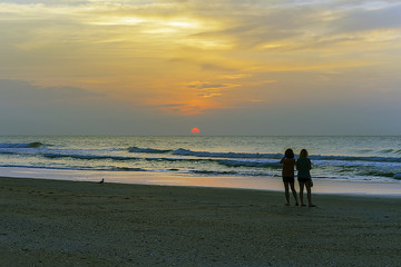 Two women on the beach looking at sunrise.
