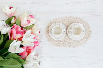 Two cup and fresh tulips on wooden table, top view.