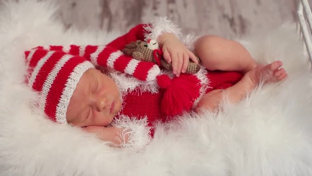 Baby dressed as Santa,sleeping on his side with his favorite toy of a deer