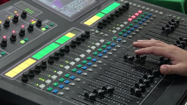 4k An audio engineer adjusts a mixer while doing live sound for a band in a concert. Mixing console is an electronic device for combining different audio signals or volume level of microphones -Dan