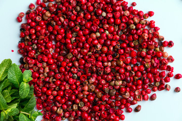 Pink peppercorns pile and fresh mint leaves on white desk. Closeup. Top view. 