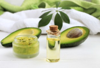 Avocado oil skin & hair care home spa. Bottle of oil, jar of mask, bathroom towel, fruit half. Green and white. 