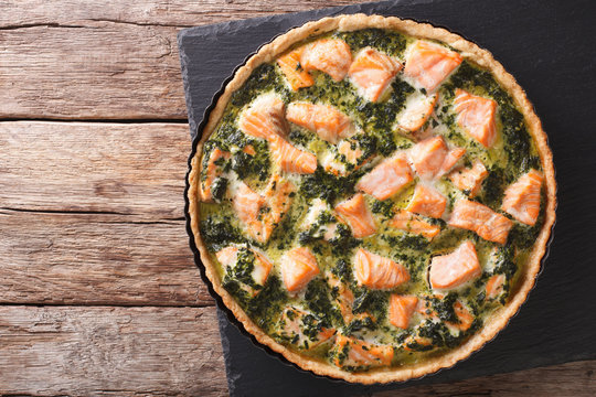 Tasty Savory Tart with salmon and spinach in the dish for baking close-up. horizontal top view