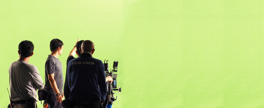 Behind the scenes of TV commercial movie film or video shooting production which crew team and photographer camera man setting up green screen for chroma key technique in big studio panorama view.