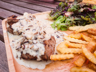 Close up steak pork with mushroom sauce, french fries and salad on wood plate.