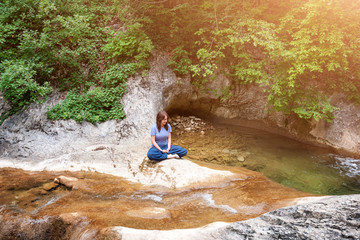 Young woman meditating in lotus position while doing yoga in a wonderful forest near waterfall. Travel, Healthy Lifestyle concept