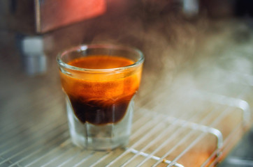 Cup of the espresso in the grid of coffee machine in a hot pair. Beautiful background.