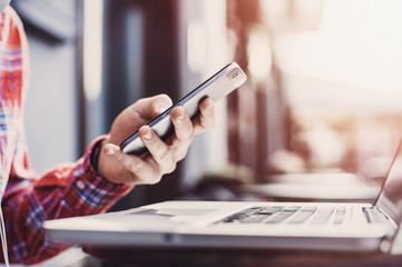 Young man texting on his smartphone in the city. Cheerful adult using mobile phone and laptop outdoors