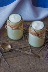 yogurt in jars on the wooden table with napkin, spoon and dried plant