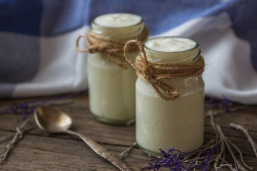 yogurt in jars on the wooden table with napkin, spoon and dried plant
