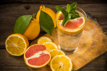 Fresh lemonade in a glass beaker with ice, green mint, red orange and lemon on the wooden table