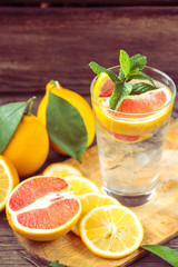 Fresh lemonade in a glass beaker with ice, green mint, red orange and lemon on the wooden table