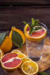 Fresh lemonade in a glass beaker with ice, green mint, red orange and lemon on the wooden table