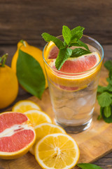 Fresh lemonade in a glass beaker with ice, green mint, red orange and lemon on the wooden table