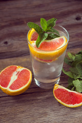 Fresh lemonade in a glass beaker with ice, green mint, red orange and lemon on the wooden table