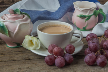 Cup of coffee with milk, red grapes, pink crockery and eustomas on wooden background