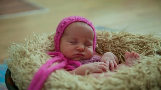 A tiny baby girl with a very nice pink hat is peacefully sleeping in a basket in the middle of a photoshoot.

