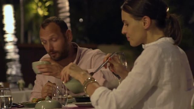 Young couple talking and eating dinner in restaurant at night
