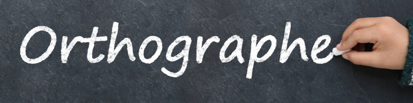Main d'enfant &eacute;crivant orthographe &agrave; la craie sur un tableau noir