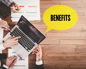 BUSINESS TEAM WORKING IN OFFICE WITH BENEFITS SPEECH BUBBLE ON DESK