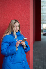 Girl teenager standing near a red wall and calling on the phone