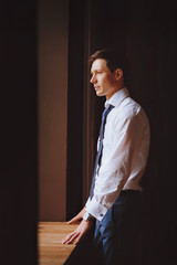 Business man looking out the window. Dressed in a white shirt and blue tie.