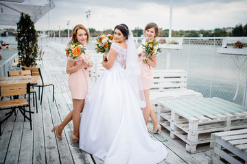 Bride with bridesmaids posed on the pier berth at cloudy wedding day.