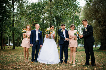 Wedding couple with bridesmaids and best mans drink champagne at park.