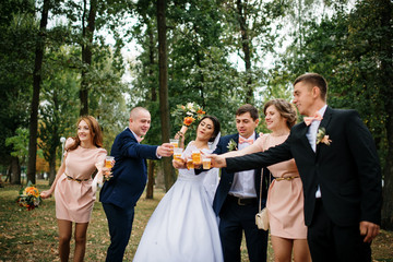 Wedding couple with bridesmaids and best mans drink champagne at park.