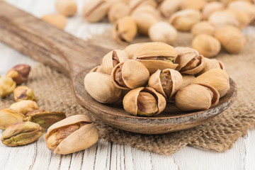 Pistachios in a wooden spoon on the old white wooden table.