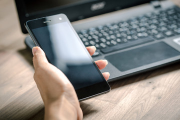 Business women hand holding smart phone to working with laptop