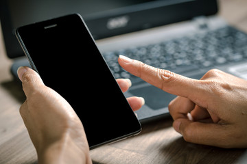 Business women hand holding smart phone to working with laptop